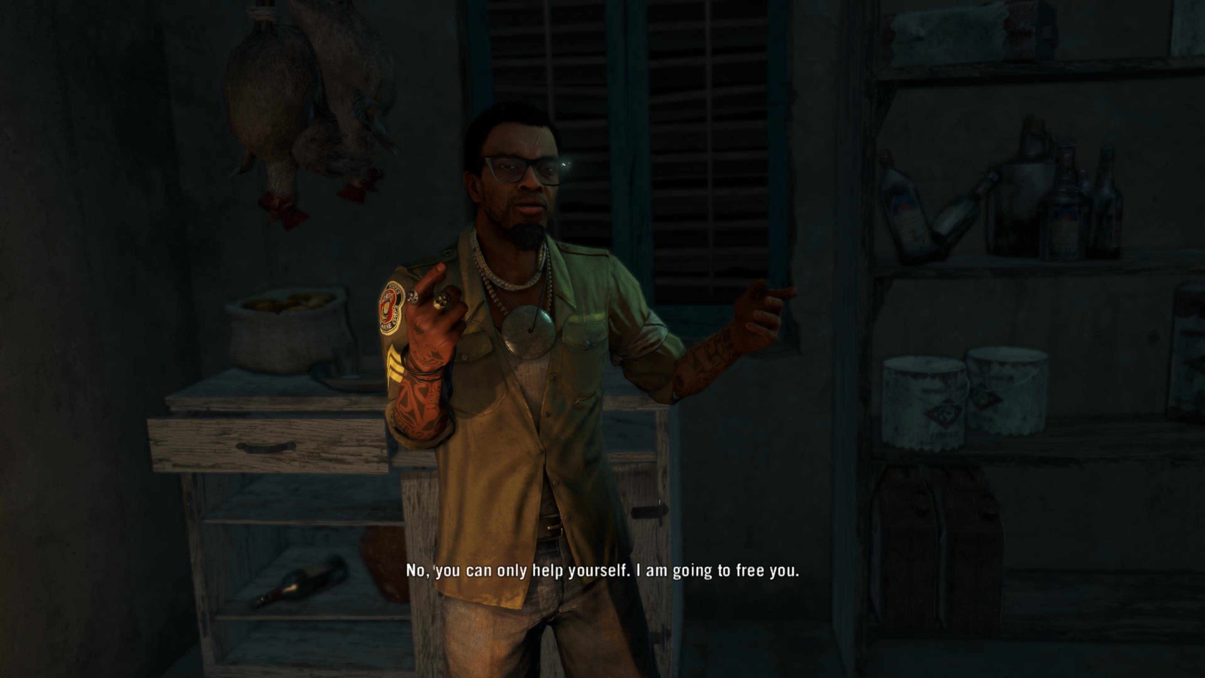 In-game cutscene showing a man standing in a dimly lit, cramped room, gesturing with his hands as he speaks. He wears glasses, layered necklaces, and a short-sleeve shirt, with tattooed arms visible. Shelves with bottles and containers line the walls, and raw poultry hangs in the background. Subtitles at the bottom read, “No, you can only help yourself. I am going to free you.”